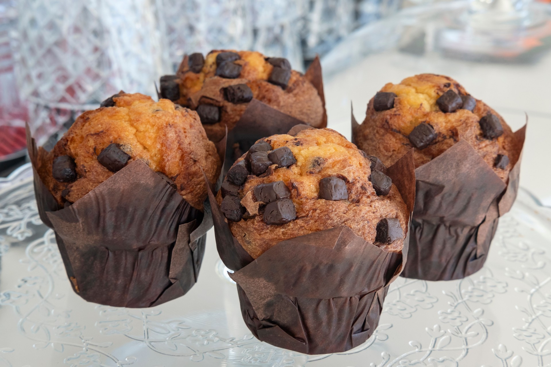 Four delectable, oversized chocolate chip muffins wrapped in parchment paper resting on a large glass plate